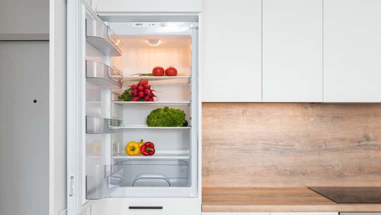 扉の開いた冷蔵庫の中に野菜がいくつか入っている画像