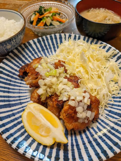 中央 鶏肉のから揚げ葱塩だれ、左上白飯、中央上 ほうれん草のアーモンド和え、右上 えのきのみそ汁の画像