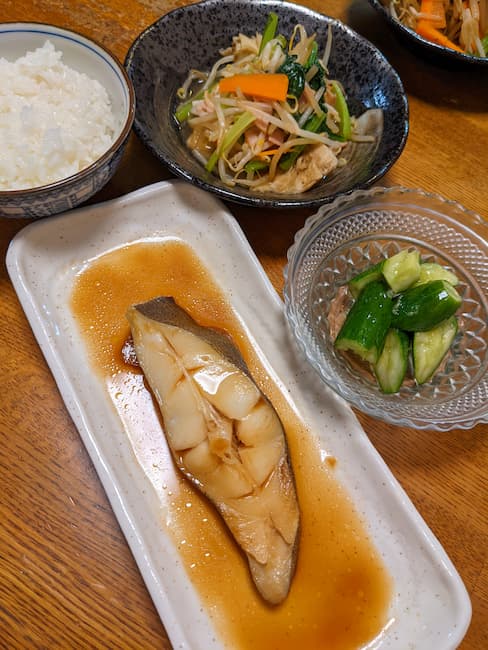 ヨシケイ定番 左下 からすがれいの煮付け、左上白飯、右上 ハムと野菜の炒めもの、右下 たたき胡瓜の画像