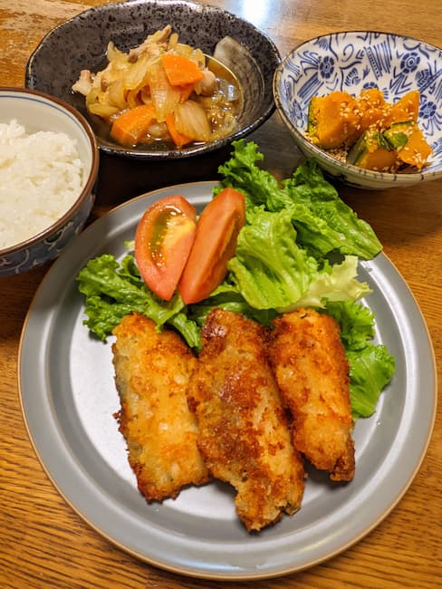 ヨシケイキットde楽のメニュー 中央サーモンのオニオンチーズフライ、左上白飯、中央上豚肉と白菜のうま煮、右上かぼちゃのごましおの画像