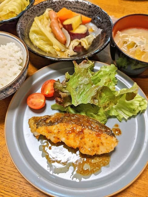 ヨシケイしき彩のメニュー 中央白身魚のムニエル、左上白飯、中央上さつま芋入りポトフ、右上みそ汁の画像