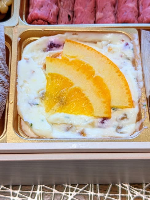 オイシックスおせち慶梅2023クリームチーズとフルーツピールの画像。上に扇形のオレンジが2切れ